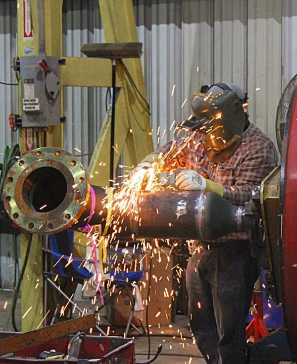 Sparks flying as a worker grinds a flanged pipe spool